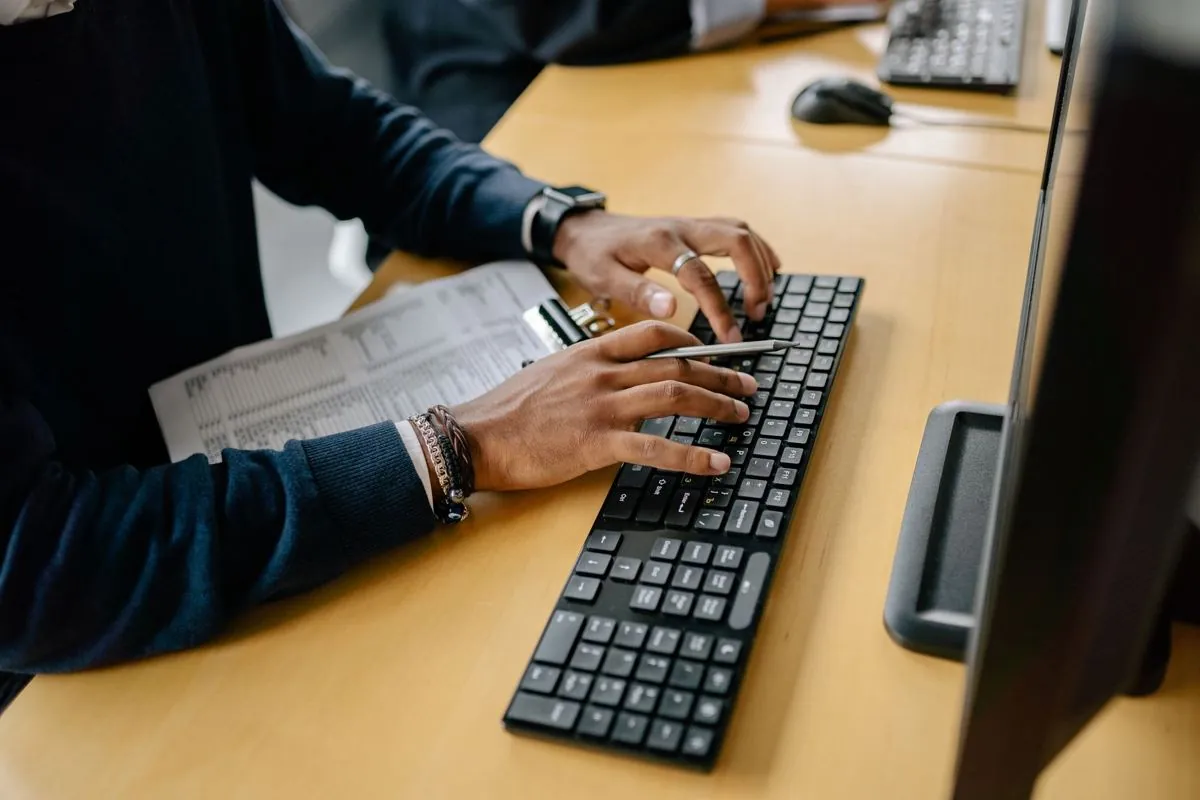 Le mani di un impiegato che digitano su una tastiera davanti a un monitor pieno di dati