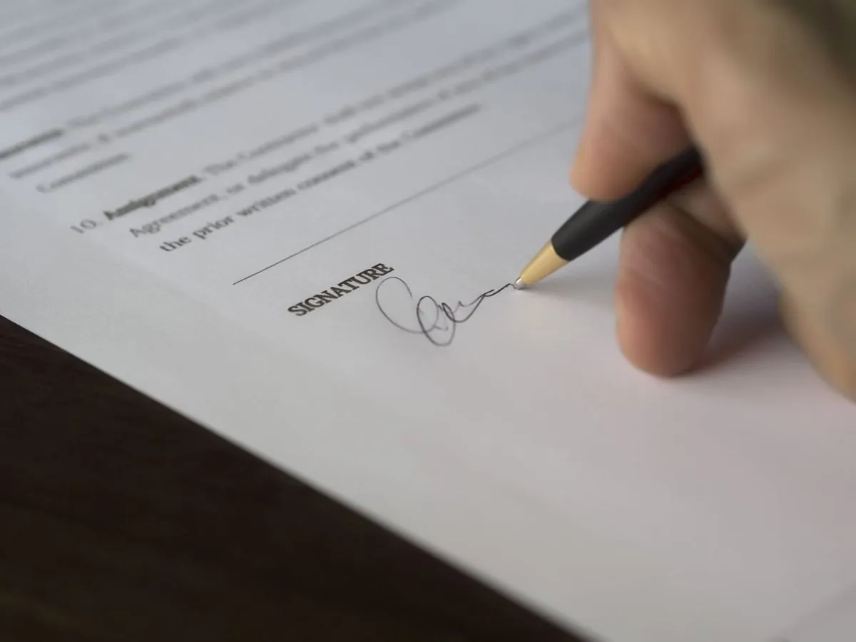 Una mano che firma l’ultima pagina di un contratto stampato sul tavolo