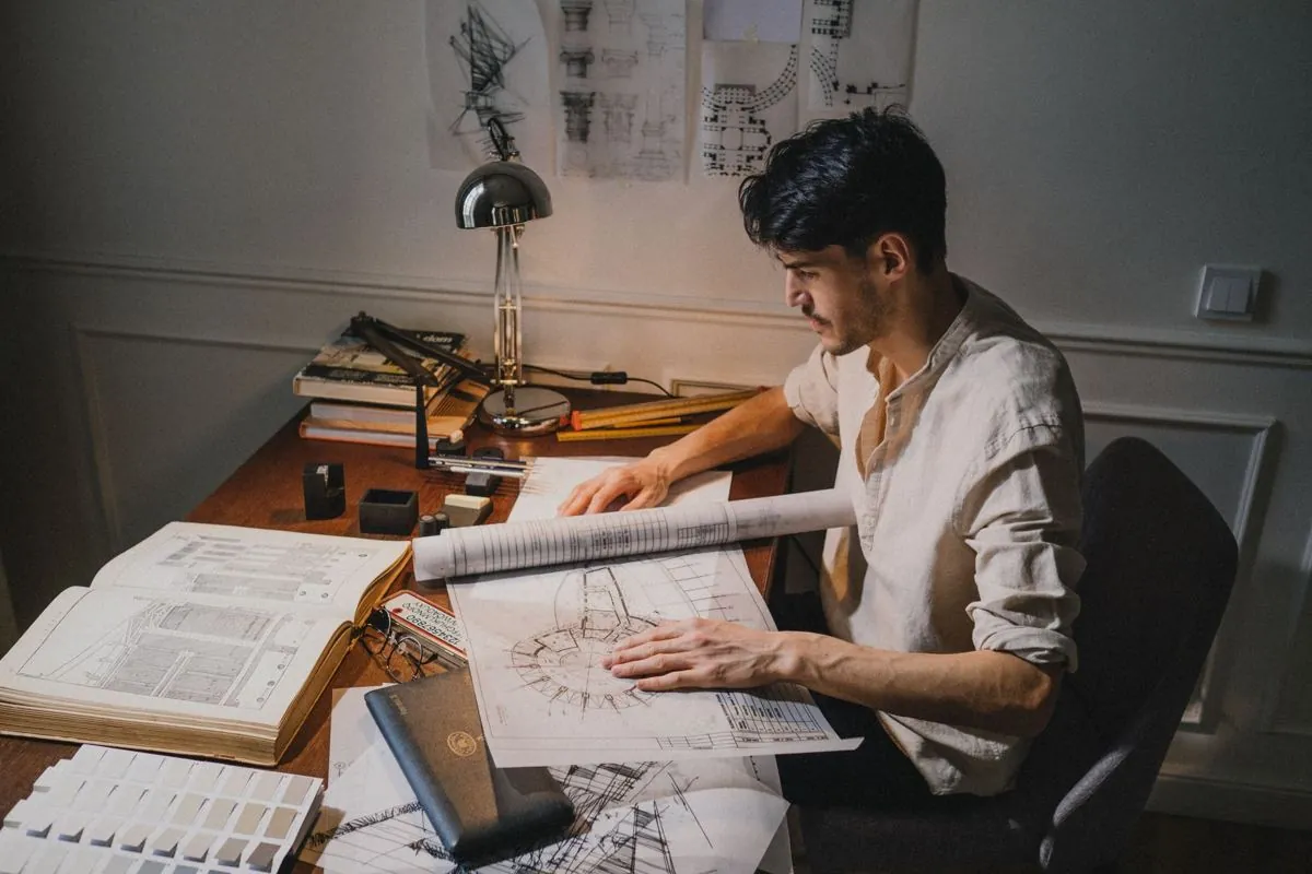 Tavolo tecnico con planimetrie stese e mani che indicano un disegno